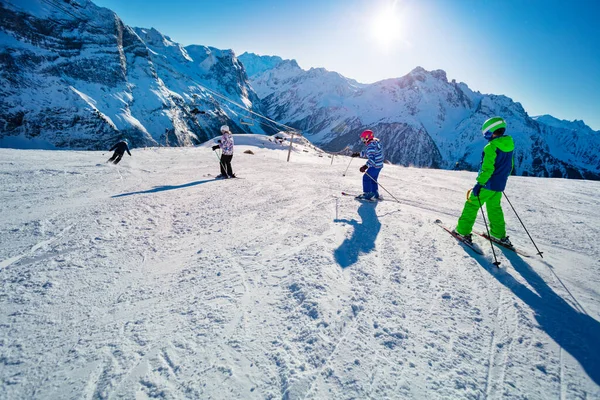 四个孩子在学校形成的阿尔卑斯山斜坡上一起滑下坡 一个接一个地从后面看去 后面是山 — 图库照片