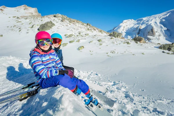 二人の幸せな女の子は スキーマスクとヘルメットの山を見て雪の上に座っている — ストック写真