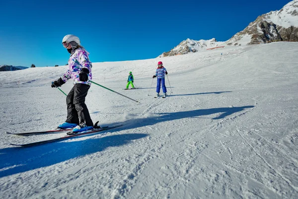 スキースクールの子供たちのグループは 幅広い簡単な斜面で次々に下り坂を移動します — ストック写真