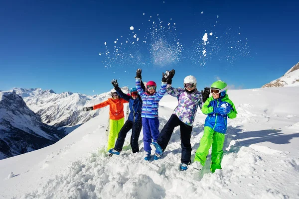 一群身穿五颜六色衣服的滑雪孩子们的有趣画像 他们一起坐在山顶上 把雪抛向空中 — 图库照片