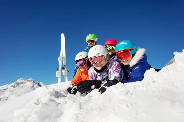 子供たちのスキークラスのグループは 山の中で一緒に雪の中に横たわって カメラを見て笑って楽しんでいます — ストック写真