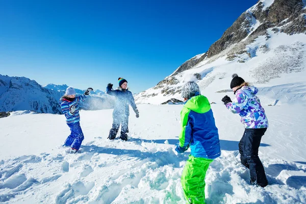 4人の子供のグループは 雪を投げ スキー衣装を着て山の中で雪合戦の冬のゲームをプレイ — ストック写真