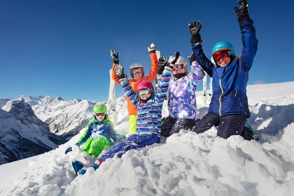 スキーの子供たちの大規模なグループは カラフルなスポーツの衣装と上昇手で山脈のピークの上に雪の山の上に座っている — ストック写真