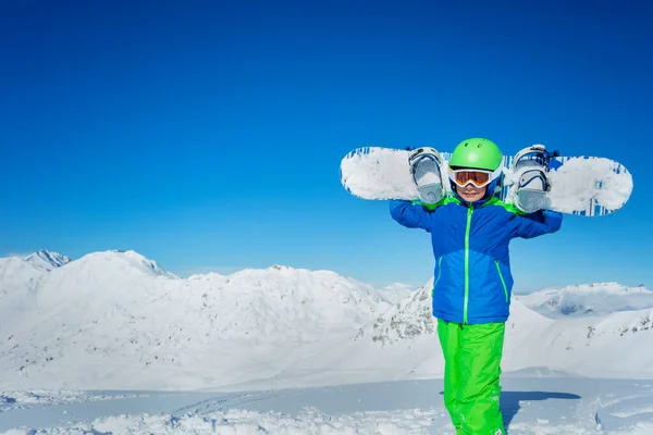 可爱的男孩站在雪地里 肩膀上拿着雪板 头戴滑雪帽 覆盖着干净的高山全景 还有复制的空间 — 图库照片