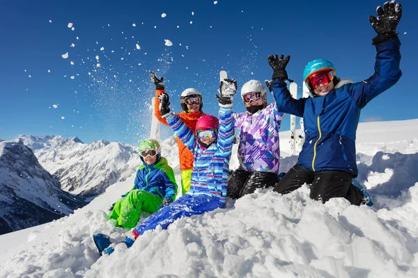 スキースクールの子供たちのクラスの肖像画カラフルな衣装で一緒に山の頂上ビューとリフトの手の上に座って空気中の雪を投げる — ストック写真