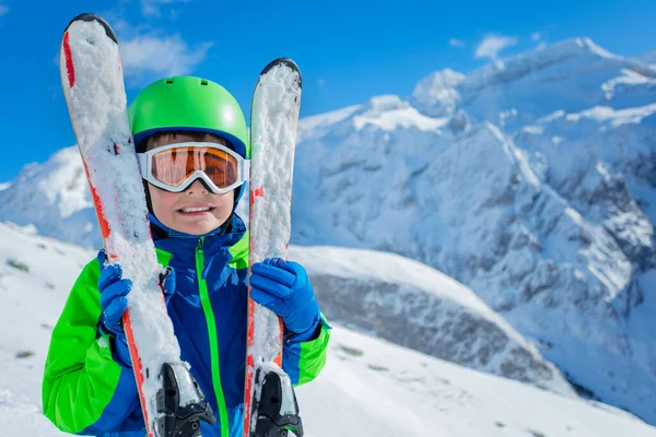 幸せな少年は山の上に立ってスキーのペアを抱いて笑顔 肖像画を閉じます — ストック写真