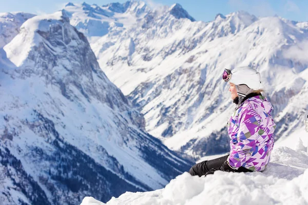 漂亮的少女身穿滑雪服 头戴安全帽 戴着面具 坐在山顶的雪地里 从后面看去 就是山谷 — 图库照片