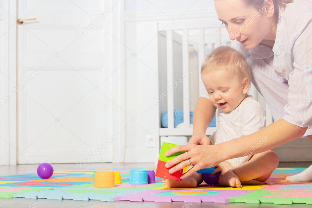Mom play with baby toddler boy building pyramids on the carpet in nursery by the child crib