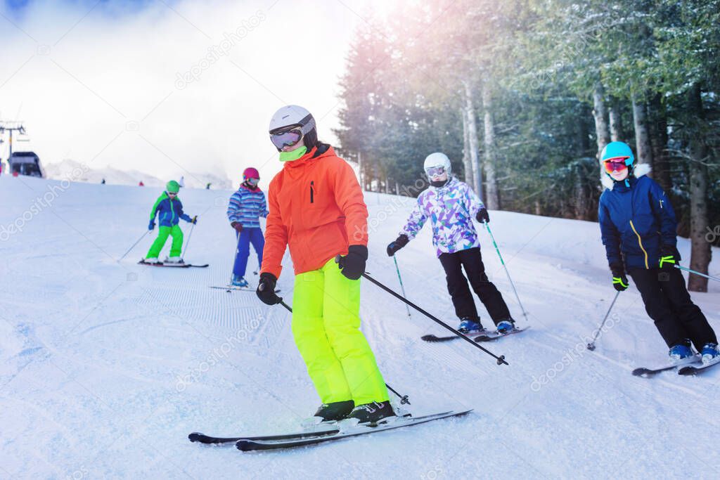 Group of children ski on the hill with friends on Alpine resort over forest on background