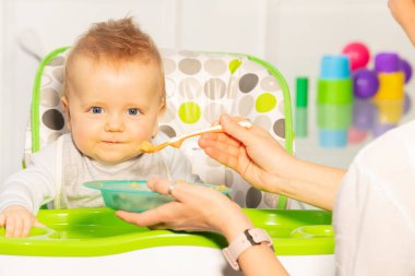Plastik tabak ve kaşıkla annesiyle yemek yiyen mutlu bir bebeğin portresi.