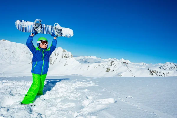 小さな男の子がマスク スキーヘルメットの側から雪の景色を手に頭の上にスノーボードを保持スタンド — ストック写真