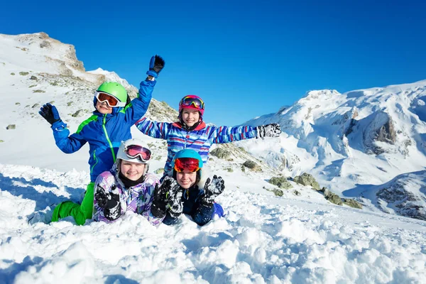4人の幸せな子供たちのグループが一緒に山の上に雪の中でスキー服の笑顔と波の手を着る — ストック写真