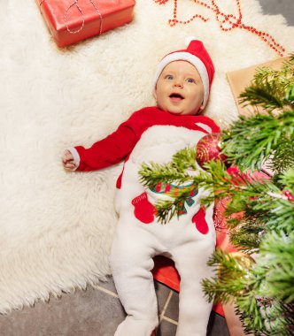 Sevimli küçük çocuk halıya uzanmış ağzı açık gülüyor ve Noel ağacının altında kameraya bakıyordu.