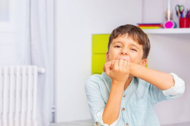Küçük otistik çocuğun yakın portresi güçlü negatif yüz ifadesiyle ellerini ısırıyor, odasında oturuyor, kendine zarar verme sorunu var.