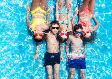 Yüzme havuzunda bir grup çocuk güneş gözlükleriyle yukarıdan su manzarası seyrediyor.