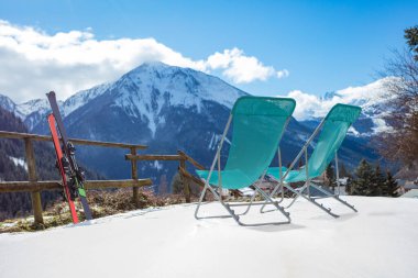 Kışın kayak merkezindeki dağ manzarası üzerinde iki çift kayak ve şezlong.
