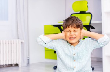 Otistik okul çağındaki çocuk. Yüzünde olumsuz bir ifade var. Kulaklarını kapatıyor ve dişlerini gıcırdatıyor.