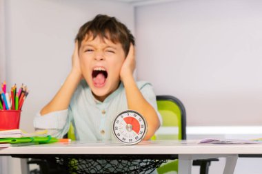 Üzgün çığlık atan otistik çocuk portresi. Kulaklarını tıka. Egzersiz sırasında egzersiz saati ve işitme sorunu olan eller kullanıyor.