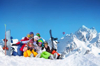 Large group of happy young adults lay in snow wave hands with snowboards and ski over mountain peaks clipart