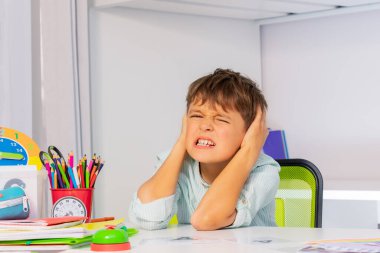Screaming sad boy with autistic disorder cover ears and grin during development therapy class lesson clipart