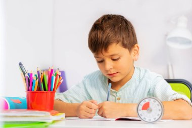 Küçük çocuk ders zamanlayıcısıyla yazma egzersizi yapıyor.