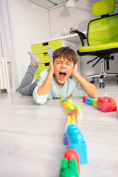 自閉症の少年は おもちゃを床の叫びに横に置き 手で耳をカバー — ストック写真