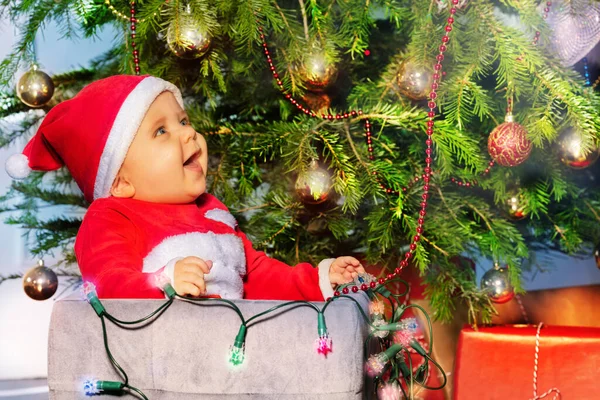 Смеющийся Мальчик Шляпе Санта Клауса Освещенными Лампами Сидит Коробке Елкой — стоковое фото