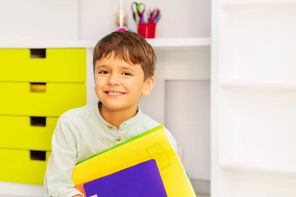 笑顔穏やかな男の子の近い肖像画で彼の部屋に座っている正の式と教科書を保持 — ストック写真