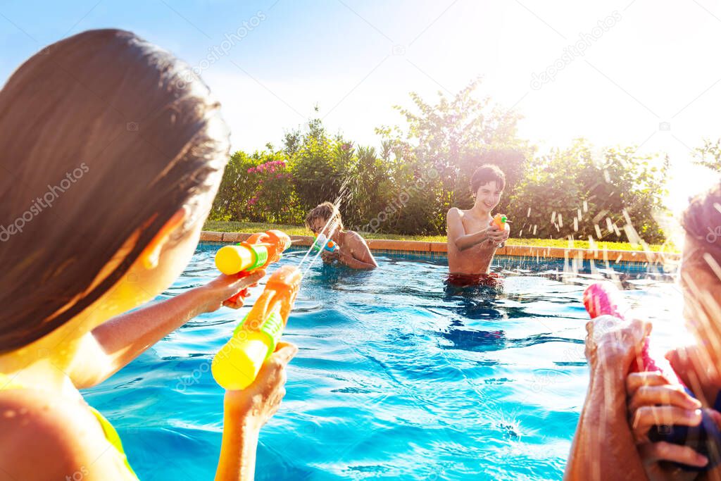 Portrait with group of children in swimming pool shooting water-gun squirt pistol on sunny day