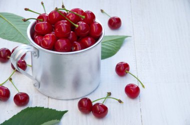 Metal bardakta olgun kirazlar. Böğürtlen topla. Metin için boşluk. beyaz tahta masa
