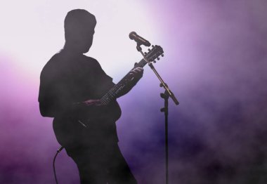 Adam gitar parlak spot altında sahnede çalmak.