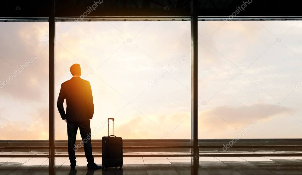 Man standing and looking out at the airport window while waiting for flight departure
