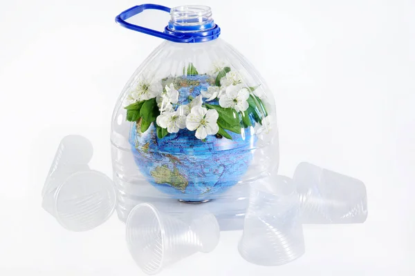 Blooming planet Earth under a plastic bottle. Around used plastic cups. Plastic garbage pollution concept. Isolated white background.