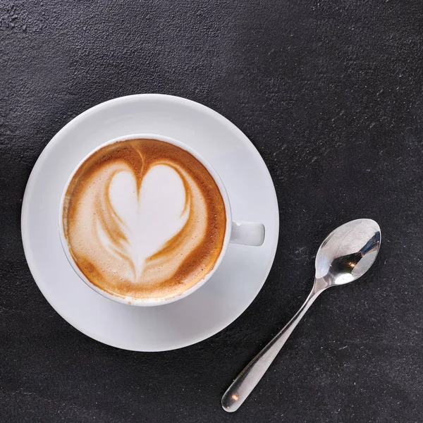 karanlık taş zemin üzerine üstten görünüm krem kapuçino Kupası bir kalp şekli ile. Kare biçimi afiş