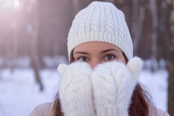 A girl in white knitted mittens and a hat. Snowy forest in the background. Winter. Snow around.