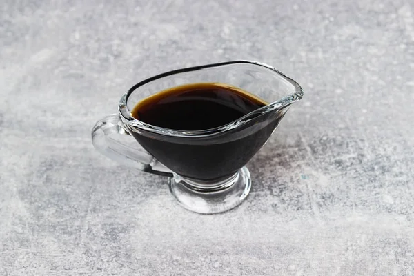 Gri arka planda cam soslu bir teknede soya sosu. Gri masada bir tabak soya sosu.