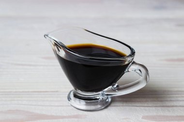 Soya sosu beyaz ahşap bir arka planda cam sos teknesinde. Beyaz ahşap masada soya sosu tabağı