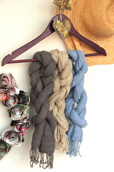 Three soft gray beyge blue cotton scarfs on a purple coat hanger with a golden heart and a star straw hat and wreath