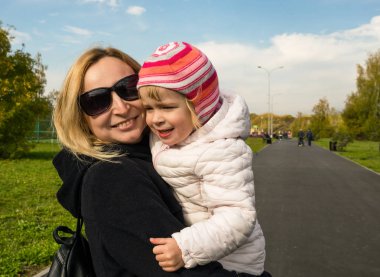 Anne ve küçük kızı parkta güneşli günde yürüyor