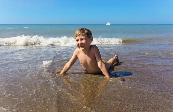 幸せな少年は晴れた日に海のビーチに横たわっている — ストック写真