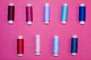 örgü işi, el işi, dikiş ve terzilik konsepti - pembe arka planda bir sıra renkli iplik makarası, düz yatak, üst görünüm