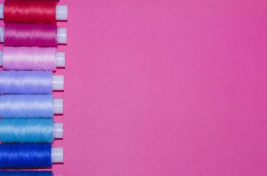 örgü işi, el işi, dikiş ve terzilik konsepti - pembe arka planda bir sıra renkli iplik makarası, düz yatak, üst görünüm