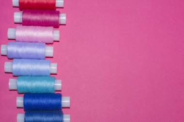 örgü işi, el işi, dikiş ve terzilik konsepti - pembe arka planda bir sıra renkli iplik makarası, düz yatak, üst görünüm