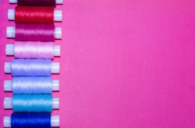 örgü işi, el işi, dikiş ve terzilik konsepti - pembe arka planda bir sıra renkli iplik makarası, düz yatak, üst görünüm