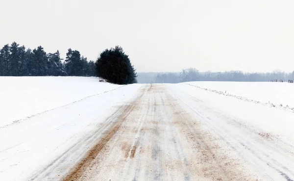 sprinkled with sand from a slip road in the winter season, traces of transport in the snow, landscape