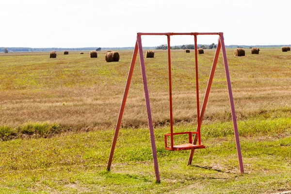 old metal swing on the field, cloudy weather in autumn or late summer