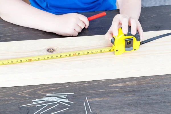 a small boy is building a wooden birdhouse, measuring the dimensions with the ruler