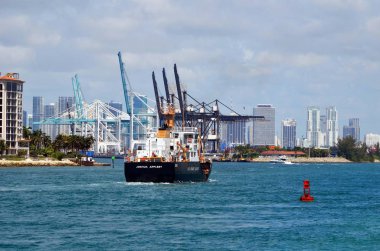 USCG Keeper sınıf kıyı şamandıra ihale Joshua Appleby Haziran 'da Miami Port içine 1, 2019. Miami uzun boylu bina silüeti ve Port Miami konteyner gemisi yükleme vinç arka planda.