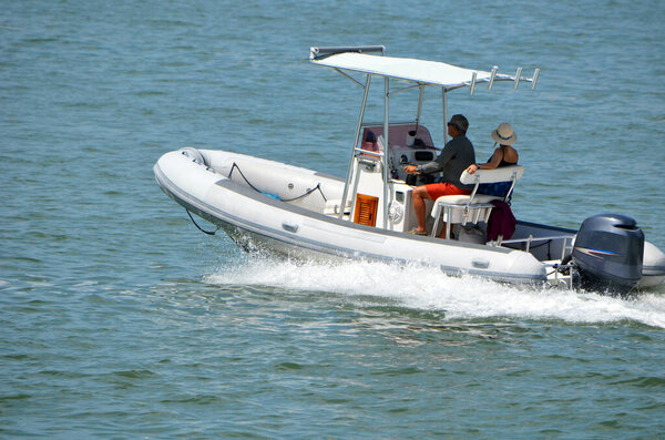 Middle aged couple leisurely cruising on Biscayne Bay off of Miami Beach in a  pontoon fishing boat with canopied center console powered by a single outboard engine.