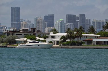 Beyaz motorlu yat Miami 'deki RivoAlto adasında lüks bir gayrimenkul ile seyahat ediyor. Arka planda yüksek bina silüeti var..
